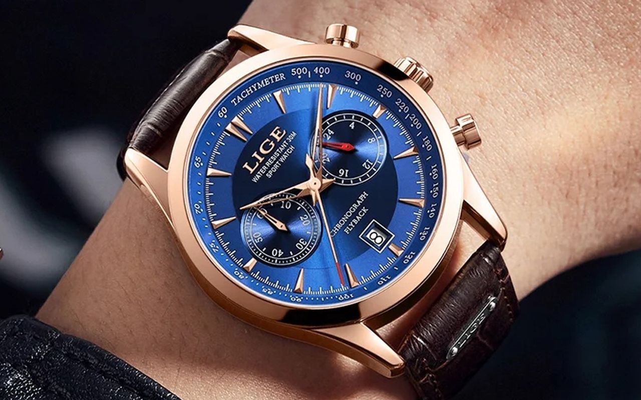 Montre Lige Chrono Flyback bleu, boitier de couleur or rose avec bracelet en cuir marron portée sur un poignet d'homme.