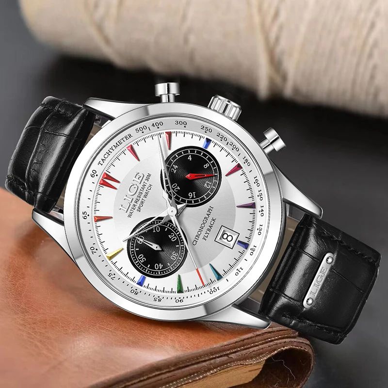 Montre Lige Chrono Flyback avec bracelet en cuir noir inclinée, reposant sur un  livre à reliure en cuir marron, son cadran et blanc et noir assorti d'un boitier et des aiguilles argenté - montre chronographe homme.