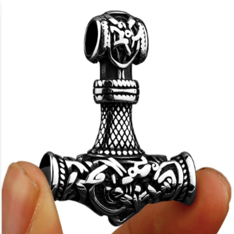 Pendentif celtique pris en photo entre deux doigts représentant le marteau du viking Thor en acier inoxydable de couleur argent