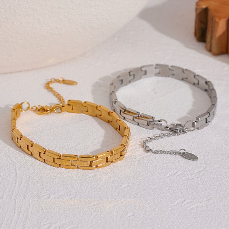 Vue sur deux bracelets à chaîne posé sur un plan de travail blanc, leurs maillons aux motif de brique, leurs fermoirs homard sont en acier inoxydable - bijoux pour femme - coloris or ou argent