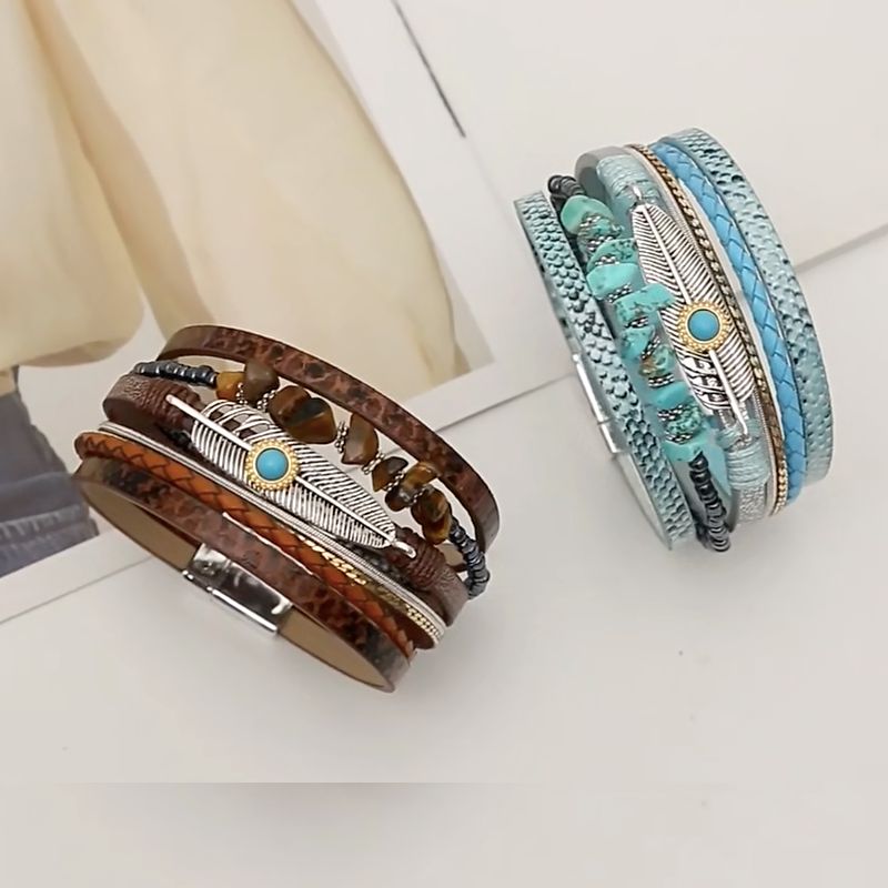 Courte vidéo sur le bracelet plume de Quetzal, on peut y voir deux wraps multilanière en cuir PU pour femme avec perle en pierre marron et bleu turquoise, son motif principal est la plume de Quetzal en alliage de zinc - fermoir magnétique.