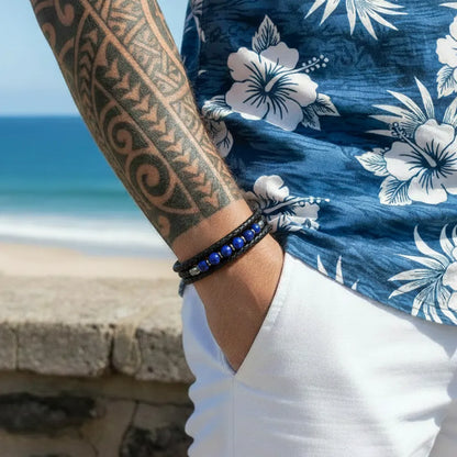 Zoom détaillé sur le bracelet Azur porté au poignet, révélant la souplesse des lanières tressées et l'élégance des six perles lapis-lazuli devant un panorama côtier ensoleillé.